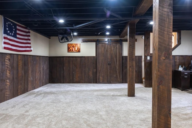 finished below grade area featuring a barn door, carpet floors, and wood walls