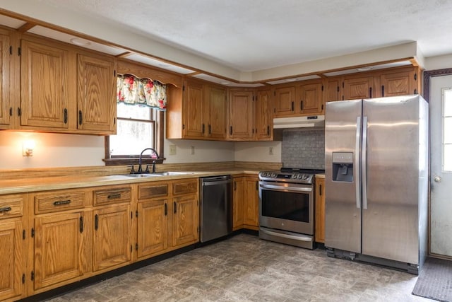 kitchen featuring a sink, under cabinet range hood, appliances with stainless steel finishes, brown cabinetry, and light countertops