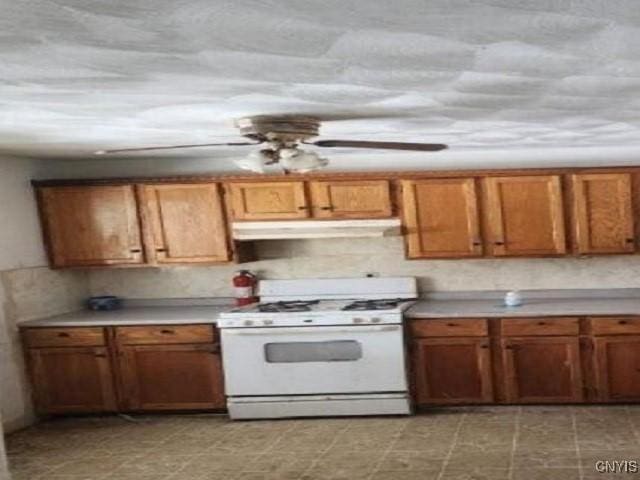 kitchen featuring under cabinet range hood, white range with gas cooktop, brown cabinetry, and light countertops