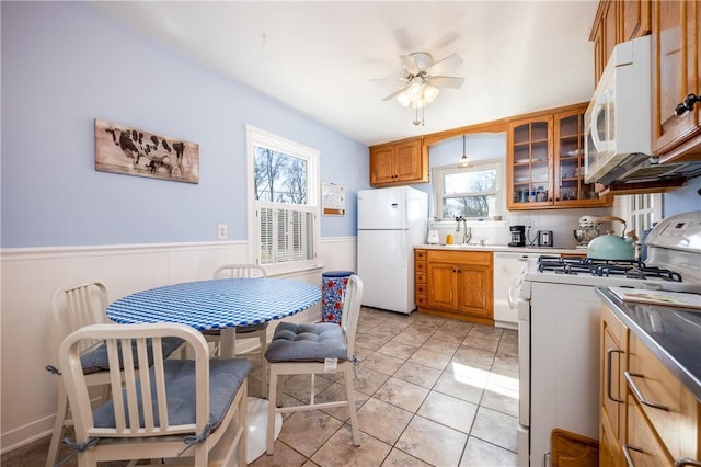 kitchen with wainscoting, white appliances, brown cabinets, and a sink