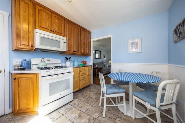 kitchen featuring brown cabinetry, white appliances, wainscoting, and light tile patterned floors