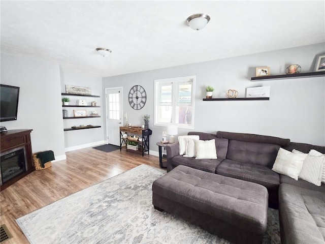 living room featuring a glass covered fireplace, visible vents, wood finished floors, and baseboards