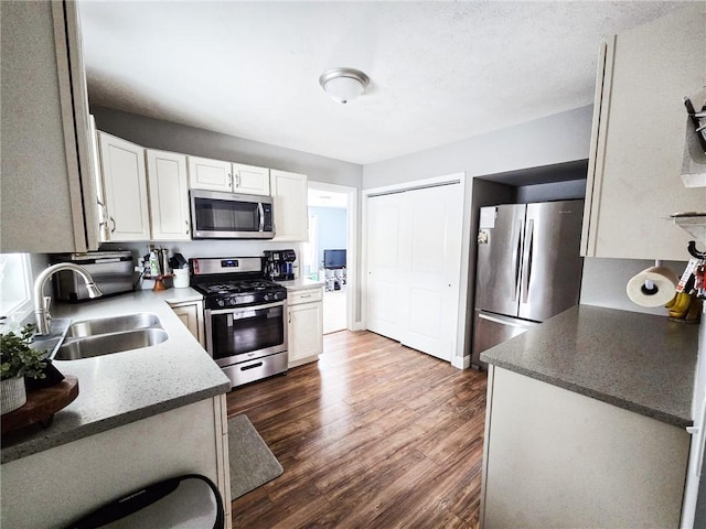 kitchen with a sink, appliances with stainless steel finishes, white cabinets, and dark wood-style flooring