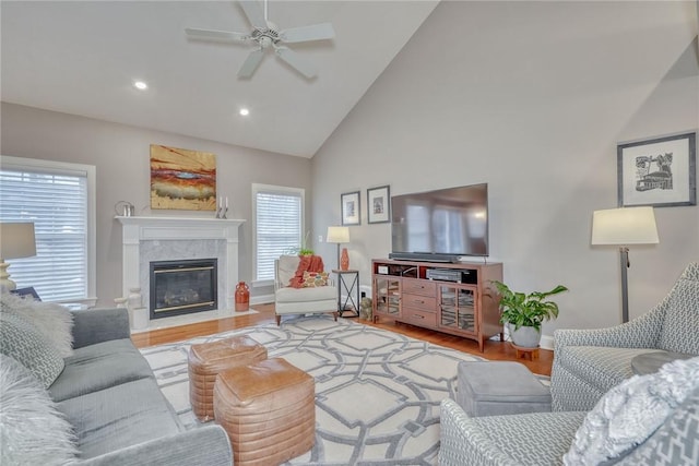 living room featuring high vaulted ceiling, wood finished floors, a fireplace, baseboards, and ceiling fan