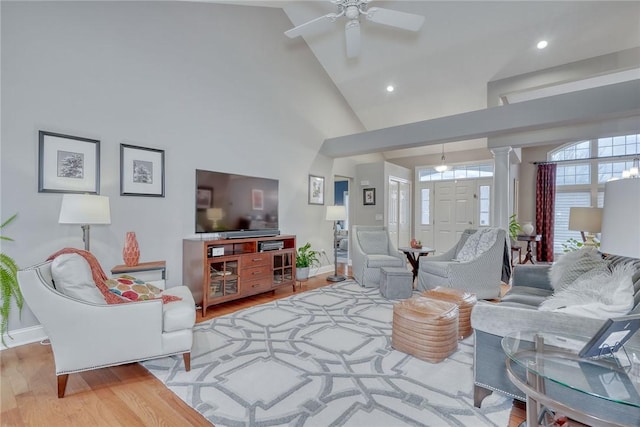 living area featuring wood finished floors, baseboards, ornate columns, high vaulted ceiling, and ceiling fan