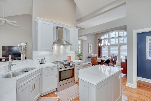 kitchen with wall chimney range hood, light countertops, vaulted ceiling, stainless steel gas stove, and a sink