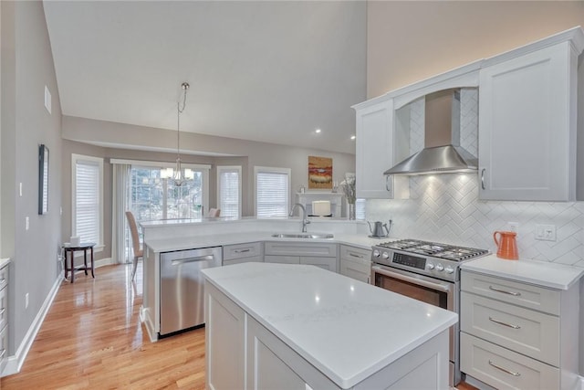 kitchen with a sink, stainless steel appliances, a peninsula, wall chimney exhaust hood, and light countertops