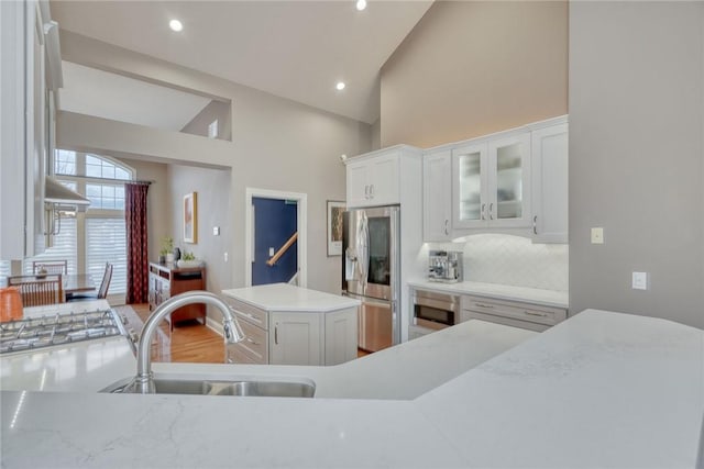 kitchen featuring backsplash, light countertops, white cabinets, stainless steel fridge, and a sink