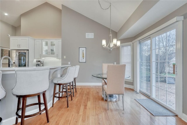 interior space featuring light wood-type flooring, visible vents, high vaulted ceiling, baseboards, and a chandelier