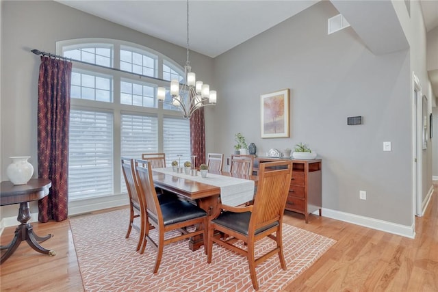 dining area featuring light wood-style flooring, a notable chandelier, visible vents, and baseboards