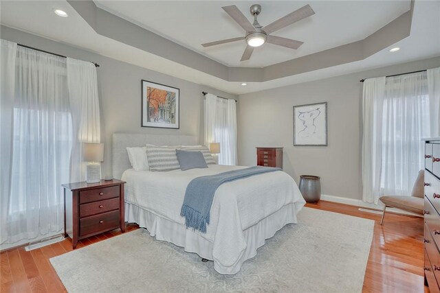 bedroom featuring a tray ceiling, multiple windows, and light wood-style floors