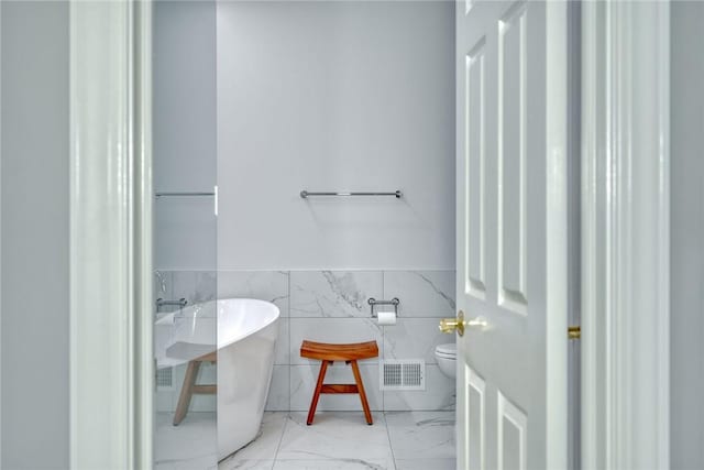 bathroom with a freestanding tub, visible vents, a wainscoted wall, marble finish floor, and tile walls