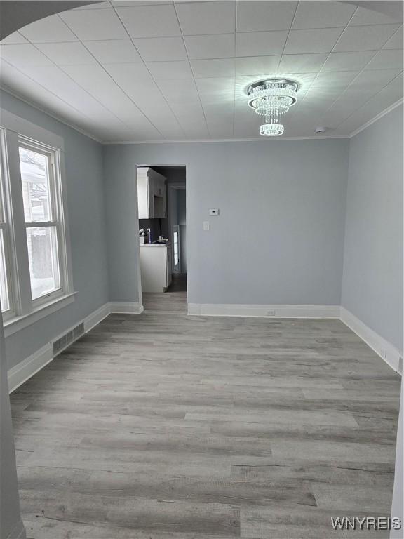 empty room with visible vents, crown molding, baseboards, an inviting chandelier, and wood finished floors