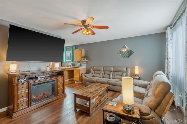 living room featuring a glass covered fireplace, ceiling fan, and wood finished floors