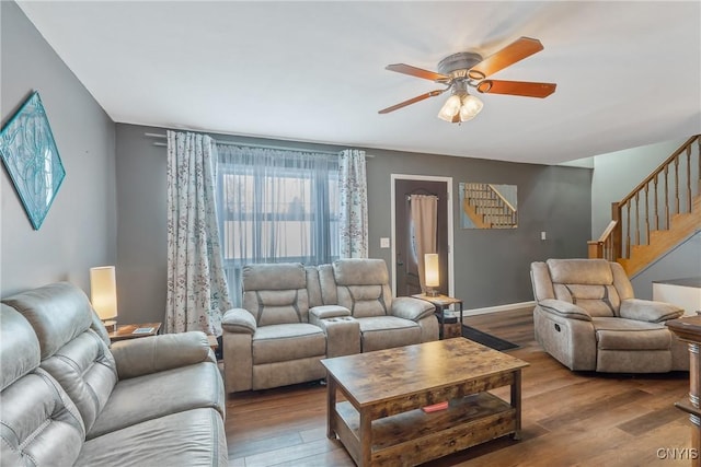 living area featuring baseboards, a ceiling fan, wood finished floors, and stairs