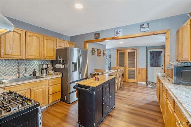 kitchen with light wood-style flooring, stainless steel fridge with ice dispenser, wainscoting, and a sink