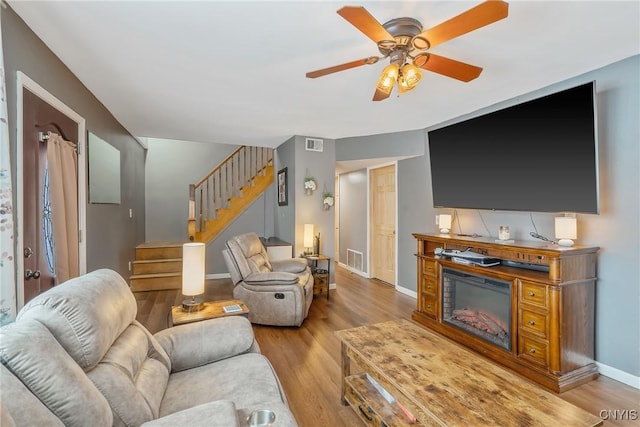 living room with visible vents, wood finished floors, baseboards, ceiling fan, and stairs