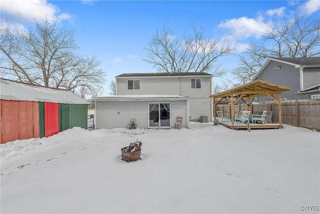 snow covered property with a wooden deck, a fire pit, an outbuilding, and fence