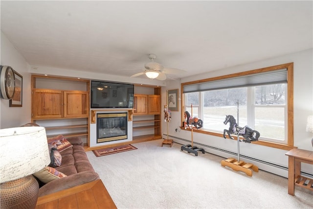 living room featuring a baseboard radiator, light colored carpet, a glass covered fireplace, and a ceiling fan