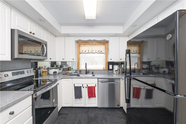 kitchen featuring a sink, white cabinetry, appliances with stainless steel finishes, light countertops, and a raised ceiling