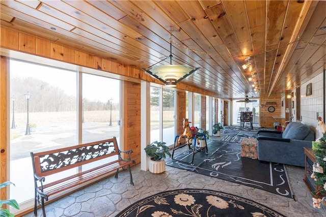 living area with a wealth of natural light, a sunroom, wooden ceiling, and wood walls