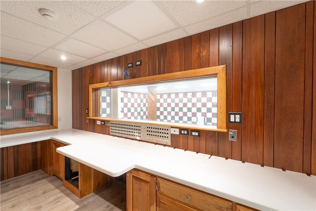 kitchen with light countertops, wooden walls, brown cabinetry, and a paneled ceiling