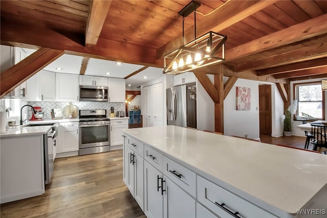 kitchen featuring wood finished floors, beam ceiling, light countertops, appliances with stainless steel finishes, and backsplash