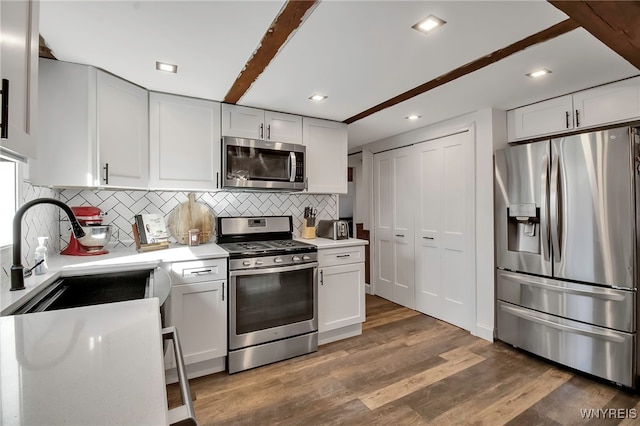 kitchen with light countertops, decorative backsplash, wood finished floors, stainless steel appliances, and a sink