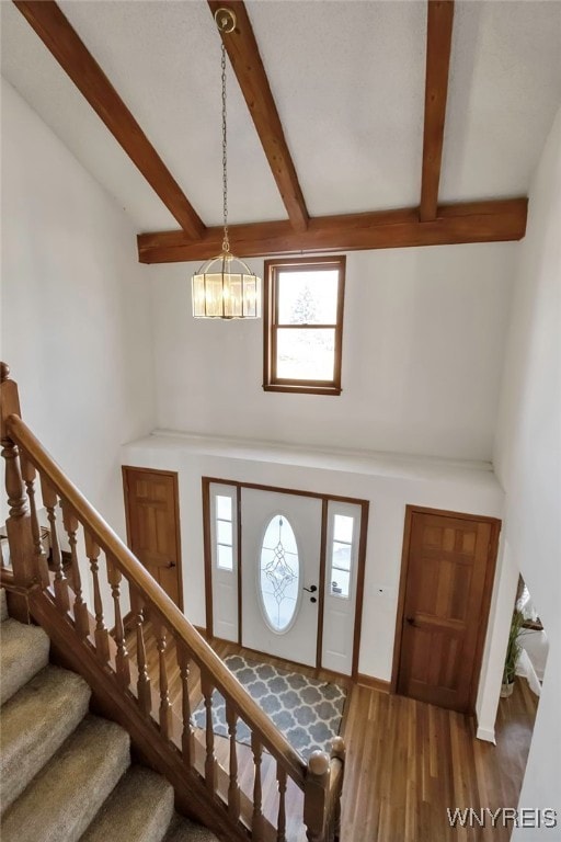 entryway featuring stairs, beamed ceiling, wood finished floors, and a towering ceiling