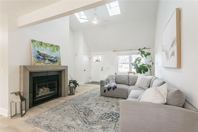 living room with wood finished floors, baseboards, high vaulted ceiling, a skylight, and a glass covered fireplace