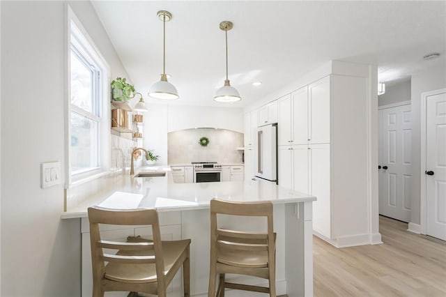 kitchen featuring light wood-type flooring, high end fridge, a sink, stainless steel range with electric cooktop, and a peninsula