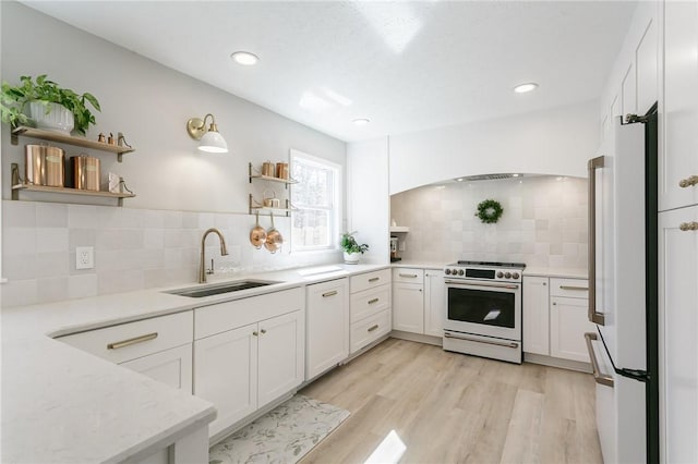 kitchen featuring a sink, range with gas stovetop, light wood-style flooring, white cabinets, and open shelves