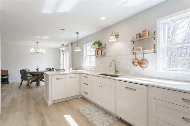 kitchen featuring open shelves, a peninsula, a sink, light wood-type flooring, and backsplash