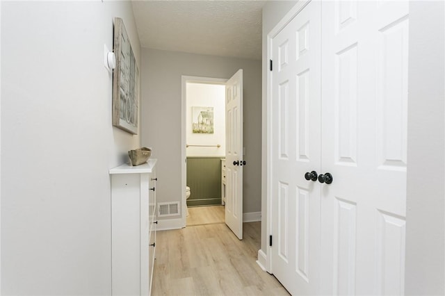 corridor with baseboards, visible vents, a textured ceiling, and light wood-style floors