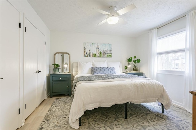 bedroom featuring a textured ceiling, ceiling fan, and light wood finished floors