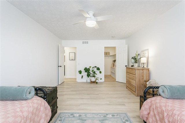 bedroom featuring visible vents, a textured ceiling, light wood-style floors, and a ceiling fan