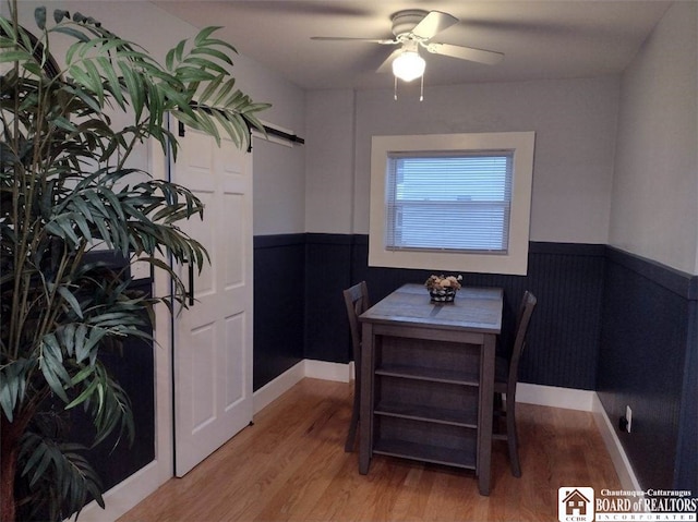 dining area featuring light wood-type flooring, a barn door, a ceiling fan, and wainscoting