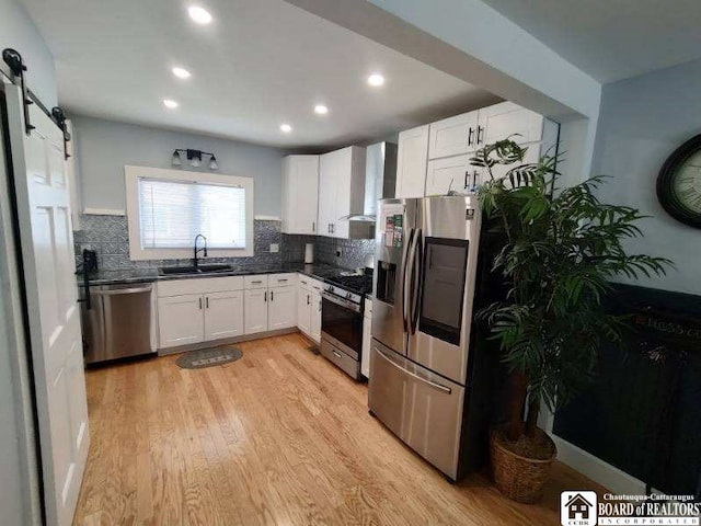 kitchen with a sink, stainless steel appliances, a barn door, light wood-style floors, and white cabinets