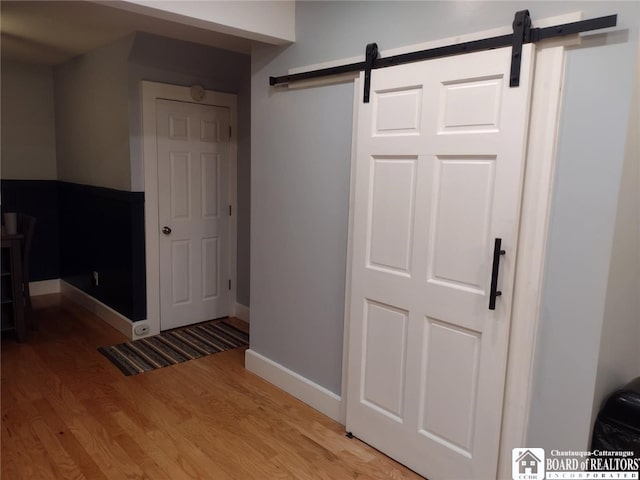 corridor featuring a barn door, light wood-style floors, and baseboards