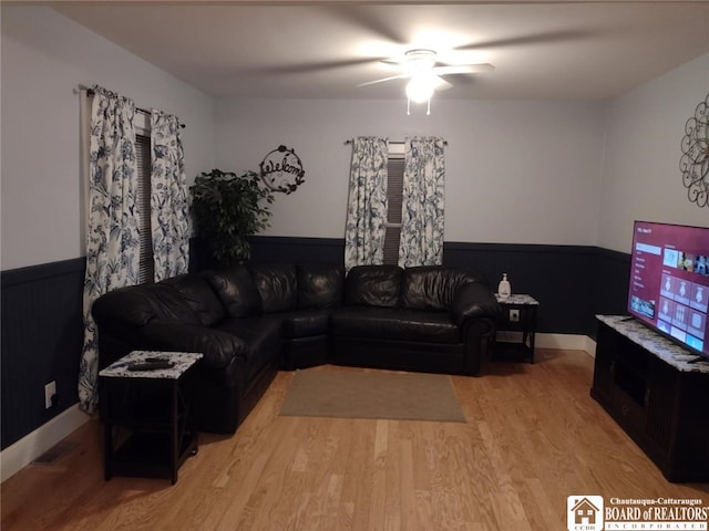 living room with a ceiling fan, a wainscoted wall, and light wood finished floors