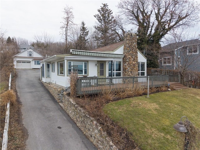 view of front of house featuring a garage, an outbuilding, a front yard, a wooden deck, and a chimney