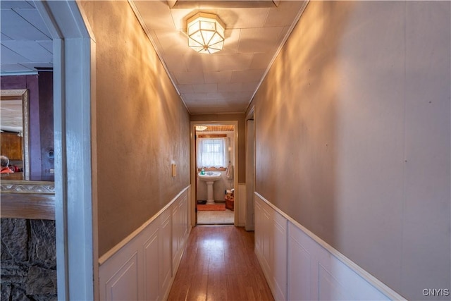 hall featuring wood finished floors, a wainscoted wall, ornamental molding, a sink, and a decorative wall