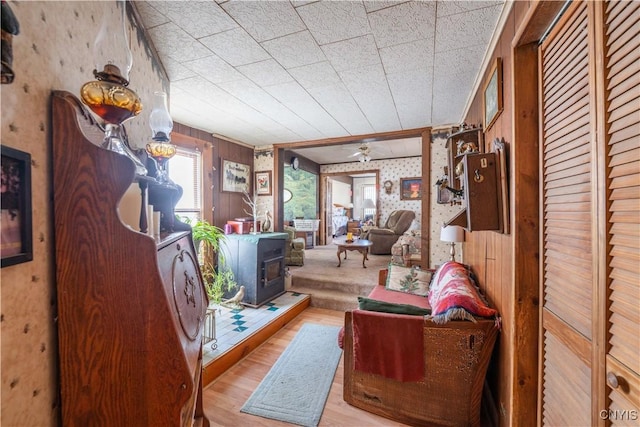 living area with wallpapered walls, a wood stove, and wood finished floors