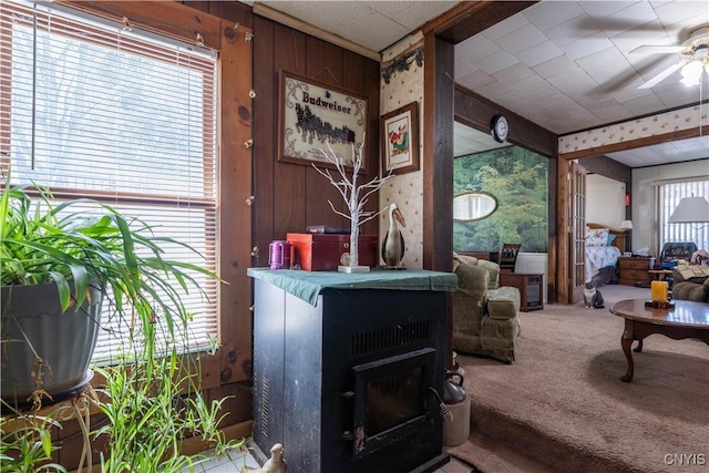 living area featuring a ceiling fan, carpet, wood walls, and a wood stove