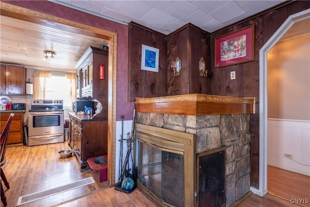 interior space with stainless steel electric range oven, a stone fireplace, a wainscoted wall, and light wood finished floors