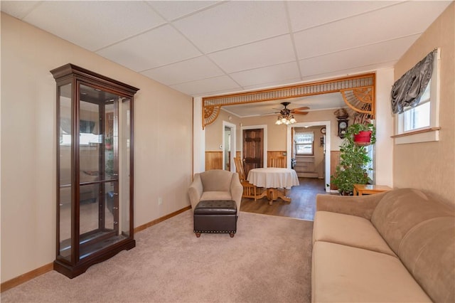 carpeted living room featuring a drop ceiling and wainscoting