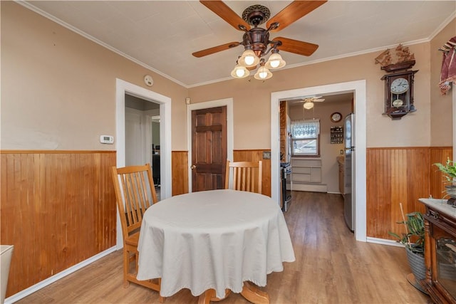 dining area featuring light wood finished floors, a wainscoted wall, wood walls, and crown molding