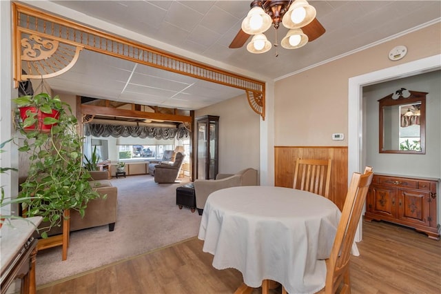 dining room featuring ceiling fan, a wainscoted wall, wood walls, ornamental molding, and wood finished floors