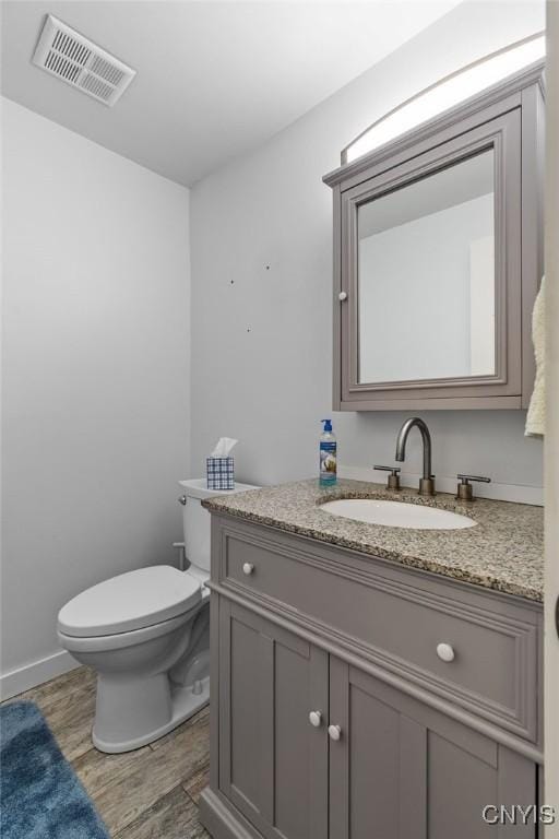 bathroom with vanity, toilet, wood finished floors, and visible vents