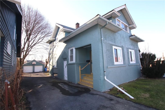 exterior space with stucco siding, a chimney, a garage, an outdoor structure, and driveway